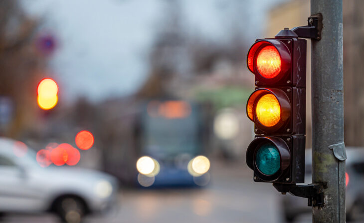 Sumea kaupunkiliikenne ja liikennevalot, etualalla semafori, jossa on punainen ja oranssi valo.