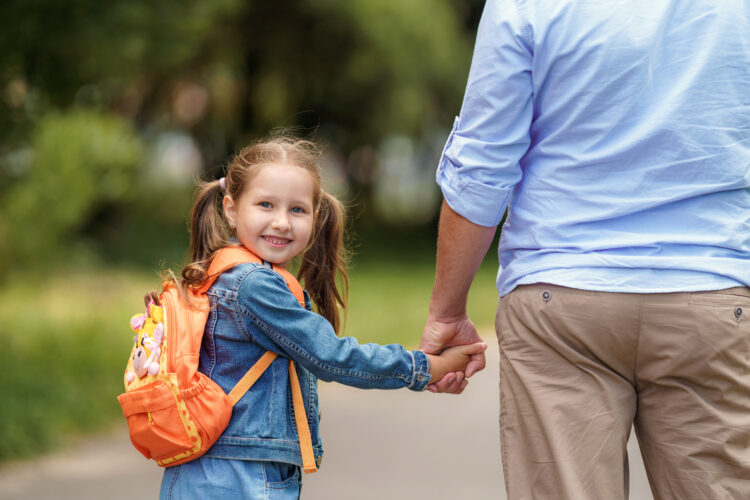A student holding a parent's hand on the way to school.