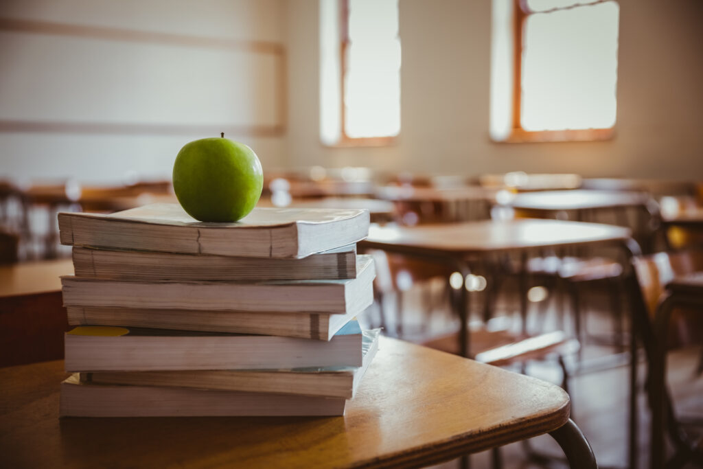 Luokkahuoneessa pulpetin päällä pino koulukirjoja, jonka päällä on vihreä omena.