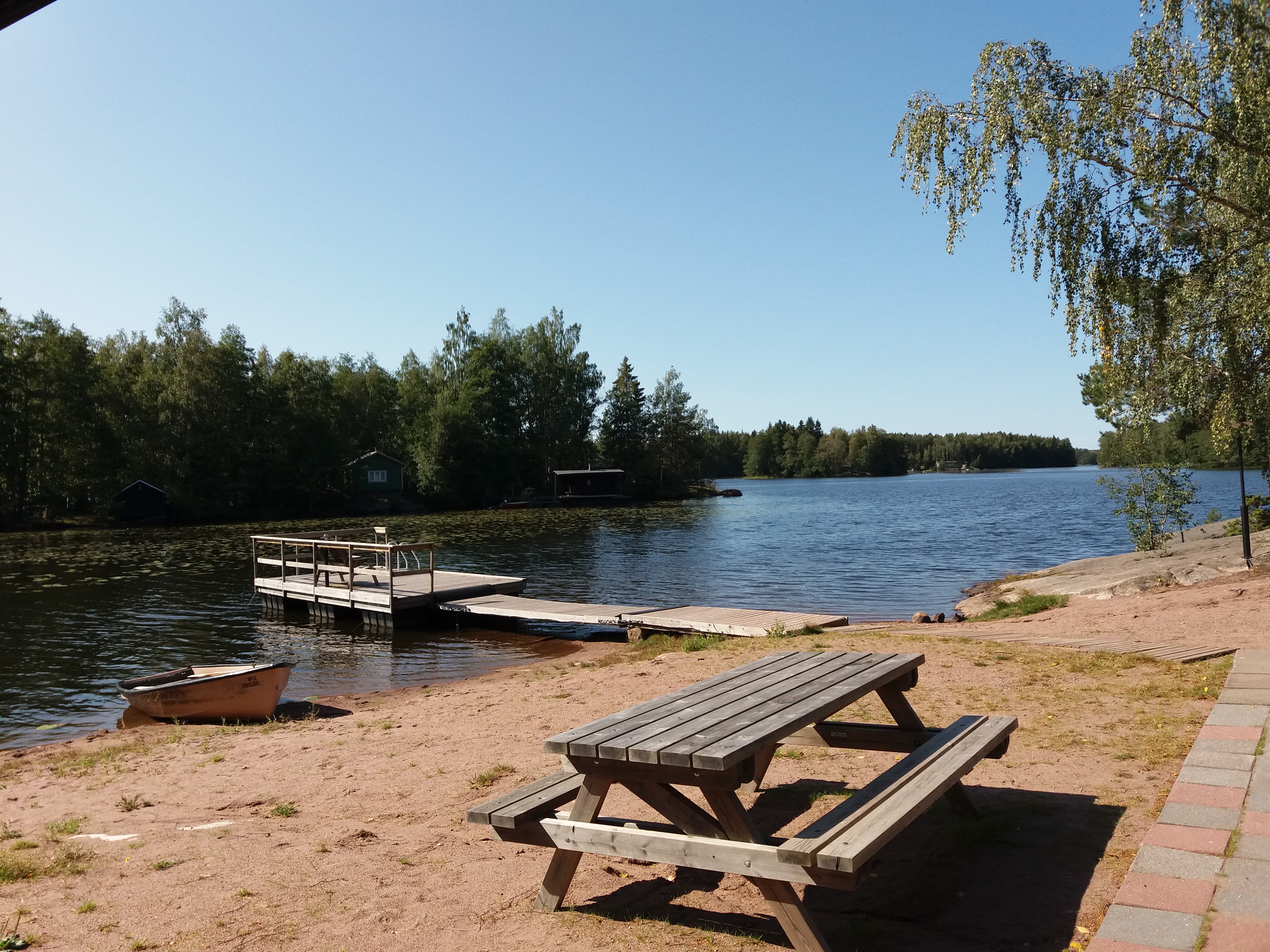 Beach Kaljasjärvi. A boat, a table with seats and a pier in the picture.
