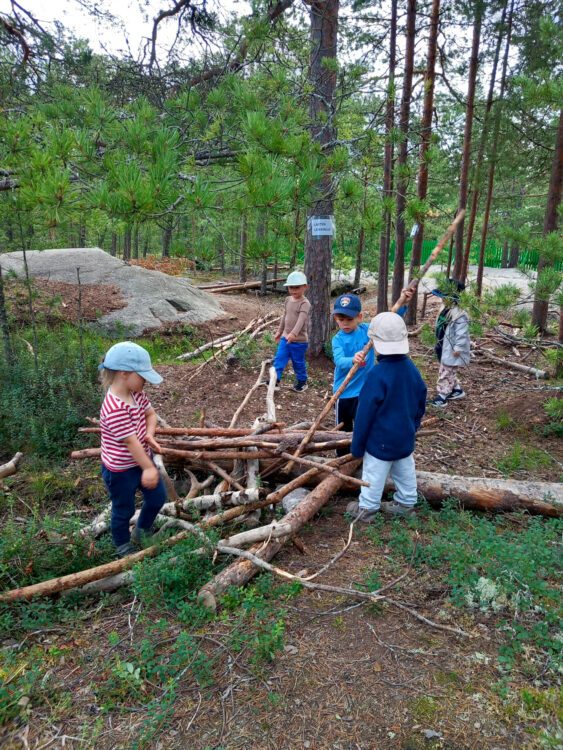 Lapset puuhastelemassa metsässä puunrunkojen parissa.